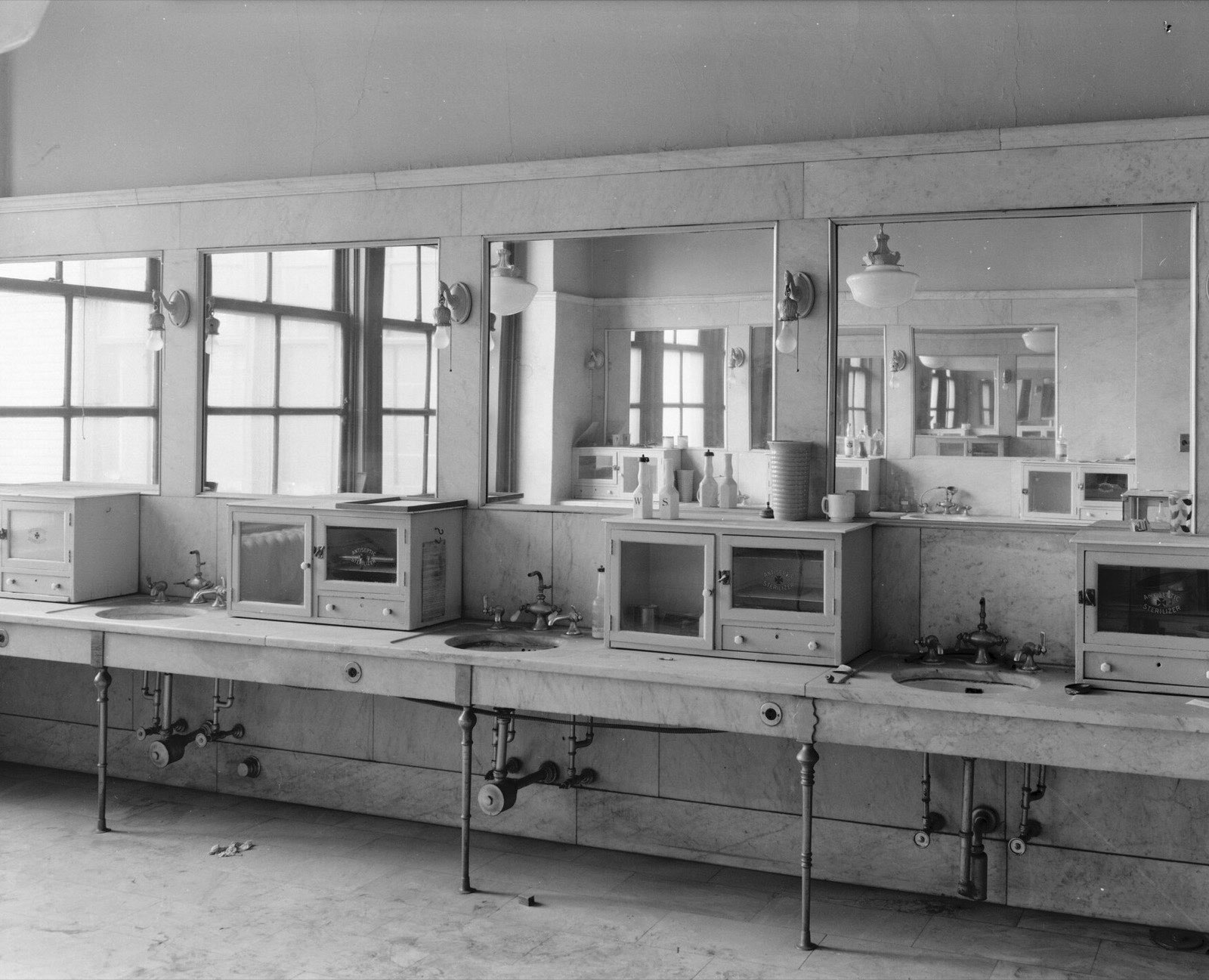A long marble counter of basins and cabinets under wall mirrors in an empty barbershop