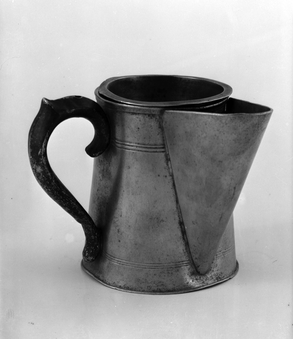 A pewter shaving mug with a spout and a curled handle