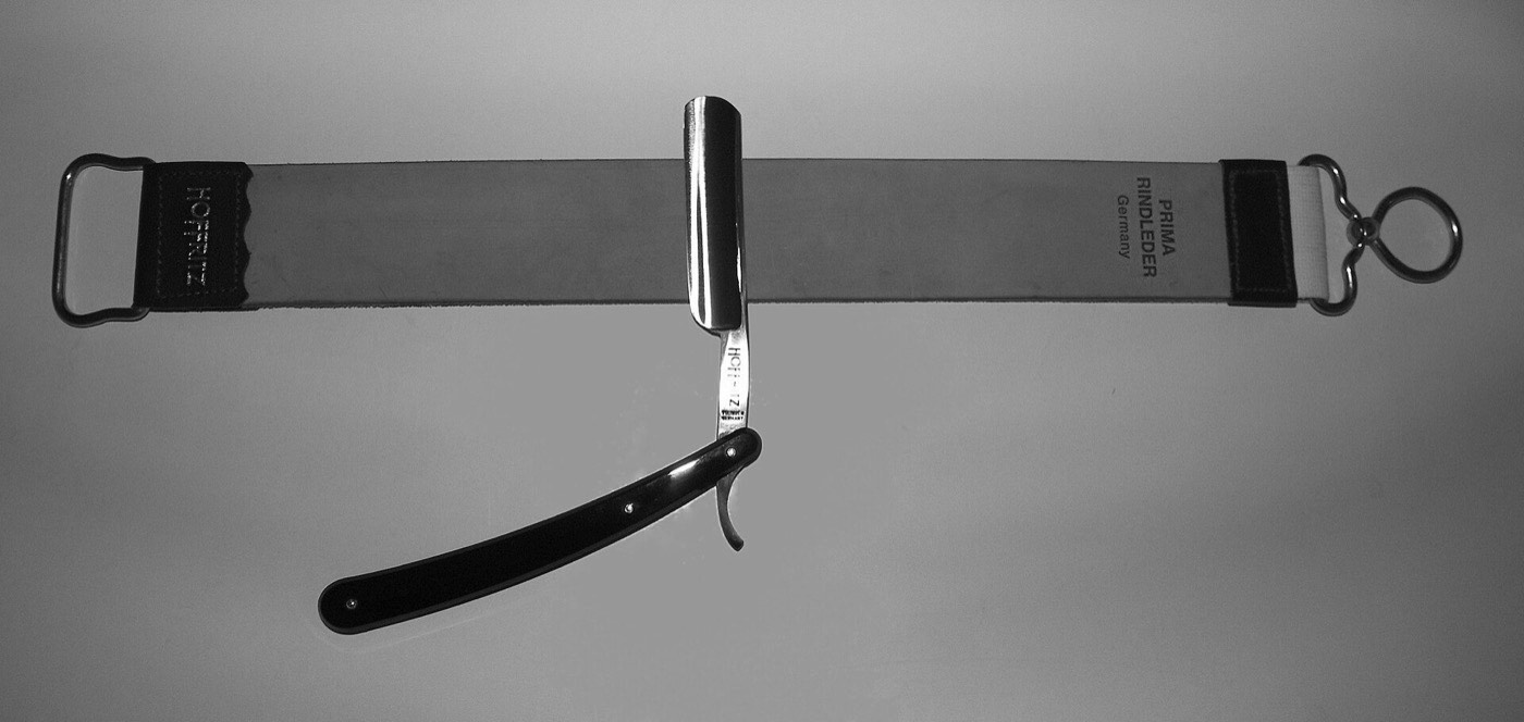 An open straight razor resting across a leather strop