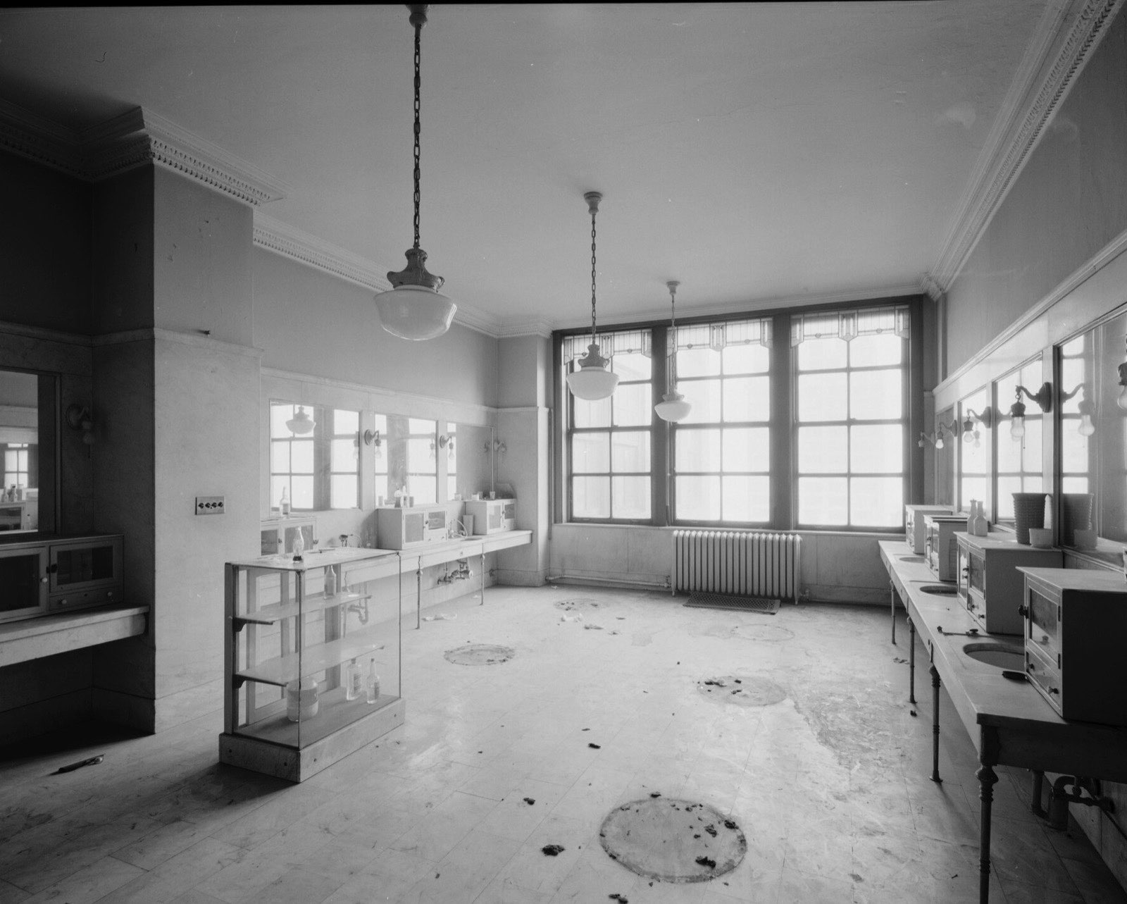 An empty, sunlit barbershop with pendant lamps, display cases and a wall of windows