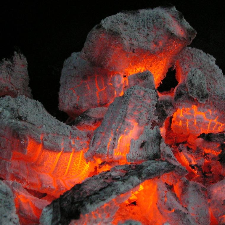 Close view of burned-down wood, grey with ash and glowing orange inside