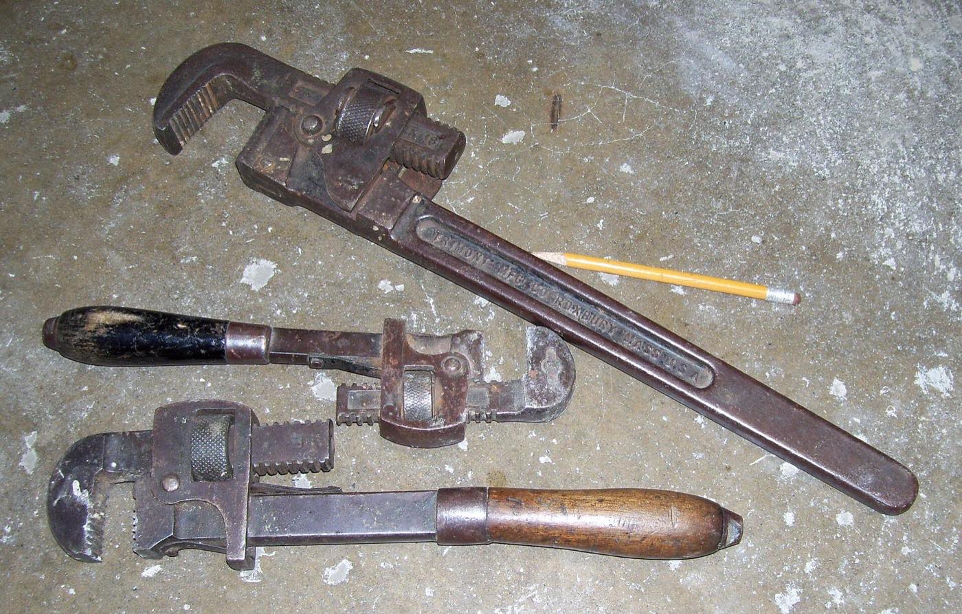 Three old pipe wrenches and a pencil lying on a concrete floor